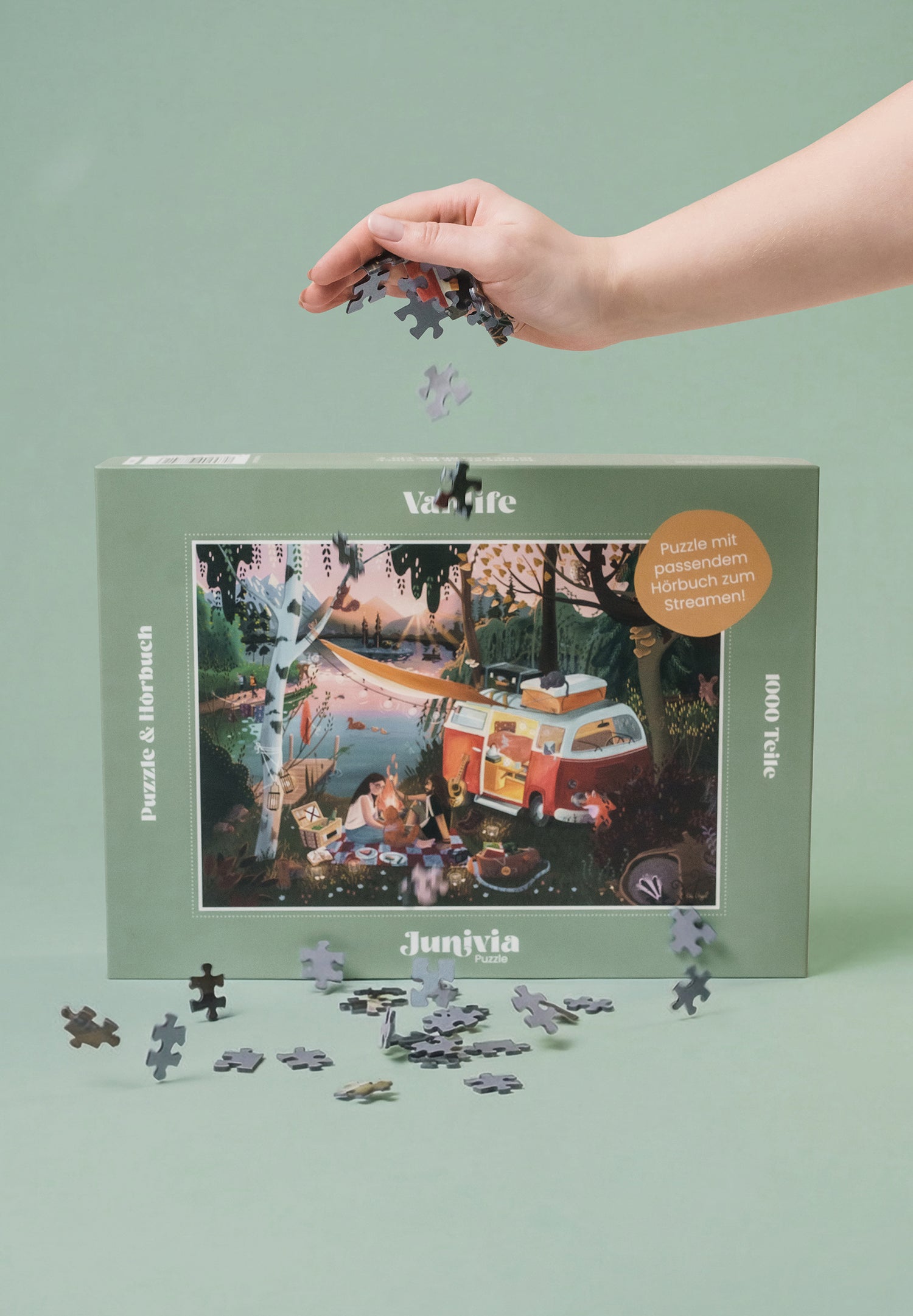 Junivia Vanlife Puzzle: Hand lässt Puzzleteile über unserem Vanlife Puzzle fallen mit Campingmotiv